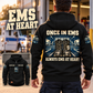 Black EMS Once and Always Vintage Hoodie worn from the back at an off-duty ambulance station, showing boots and ambulance-bay artwork, with a smaller front-view inset.