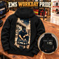 Black EMS Workday Portrait Vintage Hoodie displayed back-up on an equipment-bay bench, with kneeling-worker and ambulance artwork, a smaller complete front inset, and EMS WORKDAY PRIDE headline.