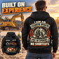 Black Excavator Operator Heritage Crest Vintage Hoodie on an off-duty man in a quiet equipment yard, showing the cream-and-orange back crest and a smaller front view with CUSTOM NAME and SINCE 2000.