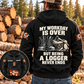 Black Logger Never Ends Vintage Hoodie shown on a back-view model at a quiet timber yard, with cream boots-and-axe slogan artwork and a smaller front inset.