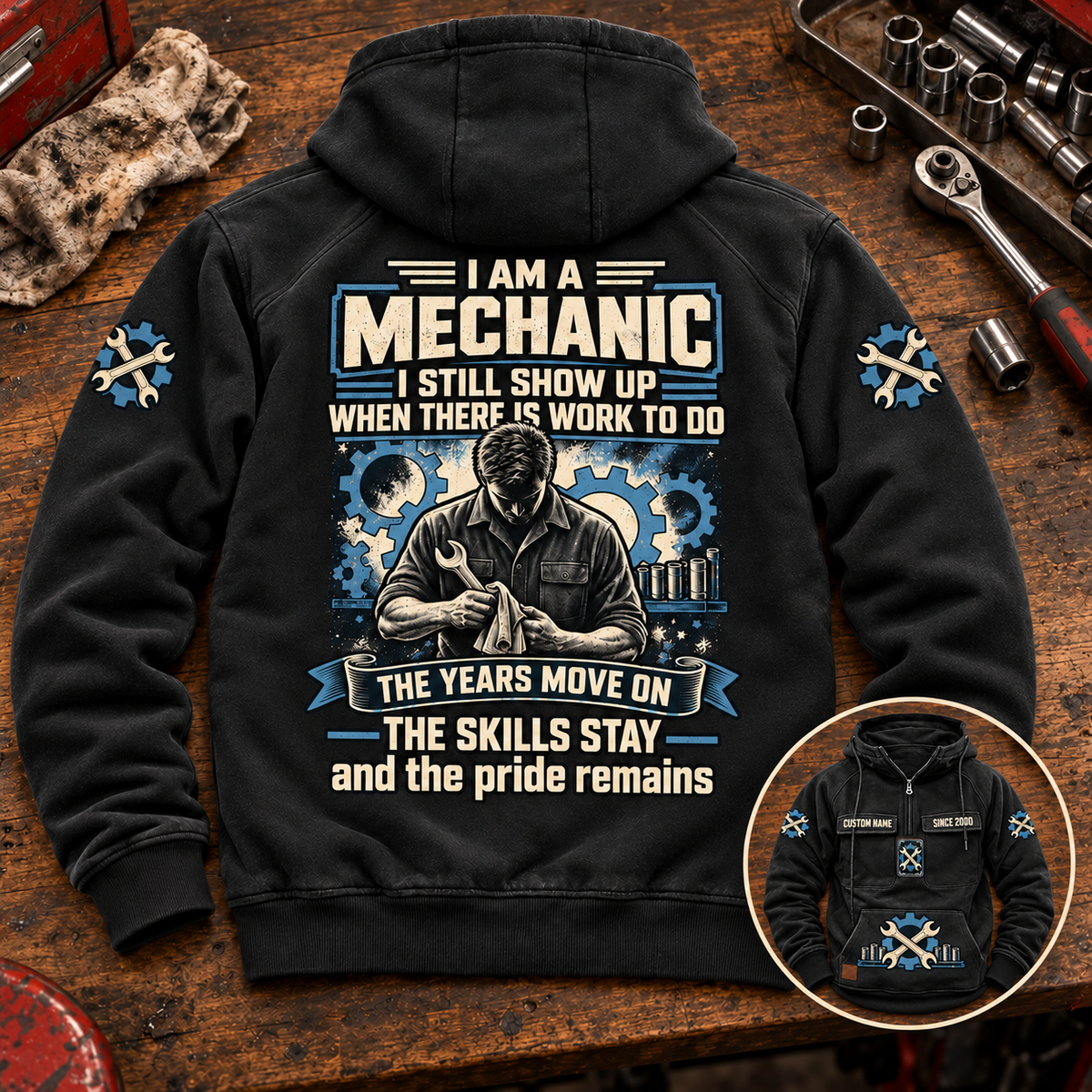Black Mechanic Skills and Pride Vintage Hoodie laid back-up on a garage workbench, with cream-and-blue mechanic artwork and a smaller front-view inset.