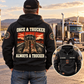Rear-view adult wearing the black Trucker Once and Always Vintage Hoodie beside a parked semi truck, with boots-and-truck back print and a smaller front-view inset.