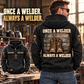 Black Welder Once and Always Vintage Hoodie shown on a model from the back in a quiet metalworking workshop, with boots and steel-plate artwork and a smaller front view showing CUSTOM NAME and SINCE 2000.