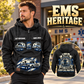 EMS Heritage Crest Vintage Hoodie in Black, front left back inset composition with faithful front and back artwork in a calm station entrance with a parked ambulance softly out of focus.