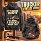 Trucker Never Ends Vintage Hoodie in Dark Gray, back left front cutout composition with faithful front and back artwork in a quiet roadside truck stop with a parked tractor cab blurred behind.