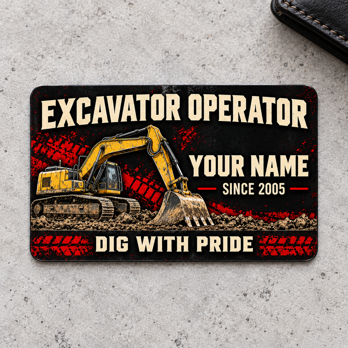 Front of the Midnight Pride Excavator Operator aluminum wallet card on a light concrete surface.