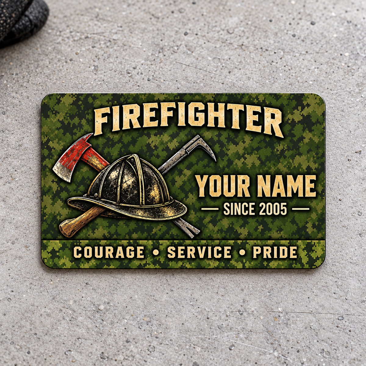 Front of olive camouflage Firefighter aluminum wallet card with helmet and crossed tools on light gray concrete.