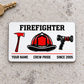 Front of white Firefighter aluminum wallet card with red and black axe, helmet and nozzle on pale concrete.