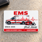 EMS Signature Classic aluminum wallet card, single front with ambulance and script name artwork on warm gray concrete.