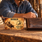 Bull Riding/Rodeo Sepia Legacy aluminum wallet card beside a closed leather wallet in a warm tack-room break scene