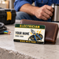 Electrician Heritage Band wallet card leaning against a brown bifold wallet on a pale concrete table