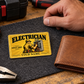 Electrician Golden Milestone wallet card on a felt work mat beside a tan leather wallet