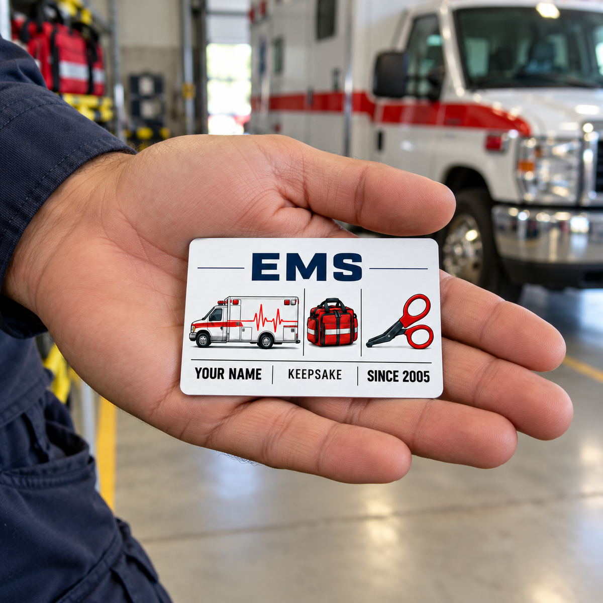 EMS Minimal Tool Grid keepsake wallet card resting in an adult male responder's open palm near an ambulance.