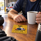 Golden Milestone EMS keepsake wallet card lying on a wooden station table beside an adult responder's hand and coffee mug.