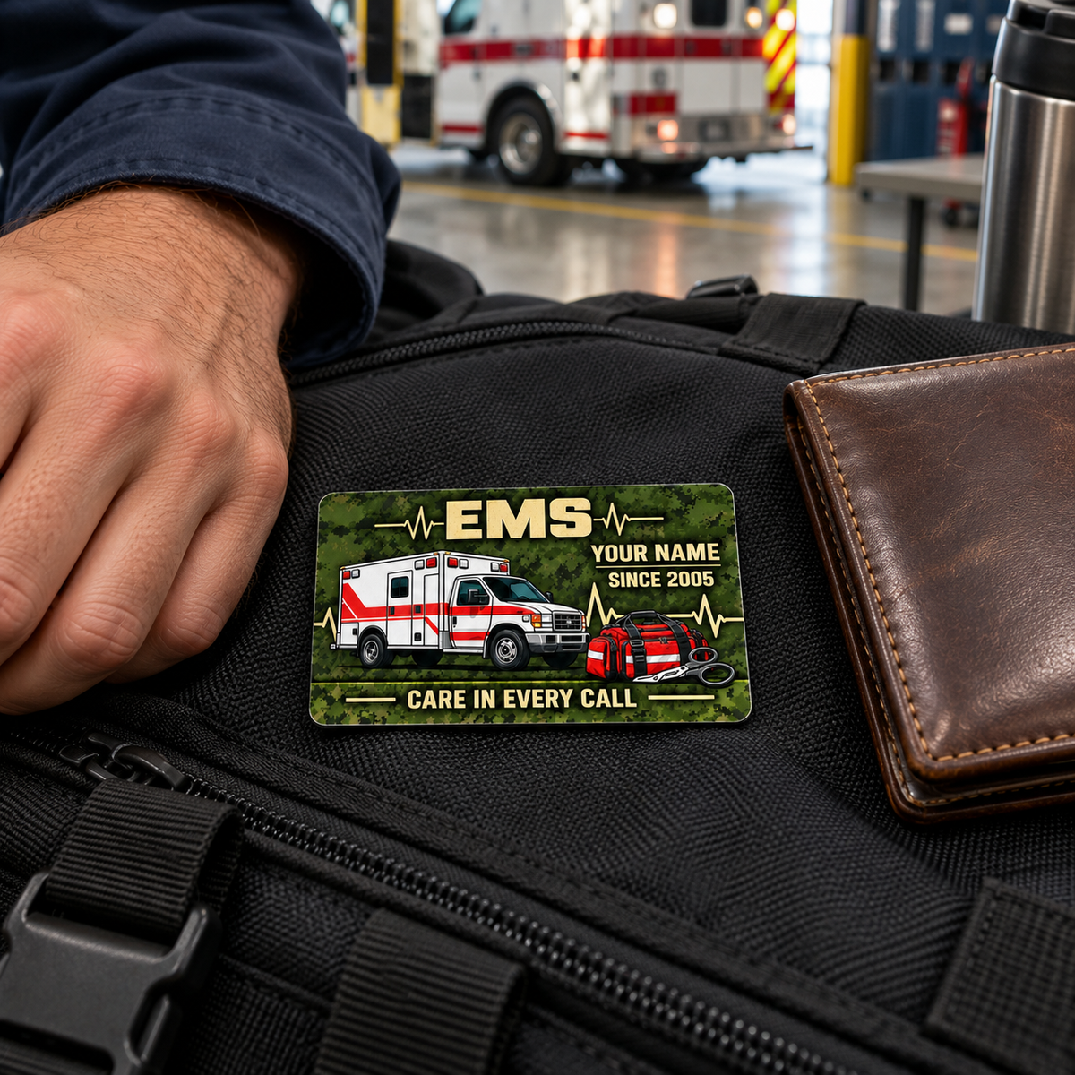Adult male responder beside an EMS keepsake card on a black gear bag, with a closed wallet and parked ambulance in the background.