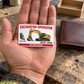 The printed front of the Excavator Operator Signature Classic aluminum wallet card shown in an occupational lifestyle setting with an adult worker.