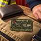 Firefighter wallet card on a tan gear bag beside a leather wallet and an adult man's resting hand.