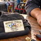HVAC Ivory Heritage aluminum wallet card resting on a folded work jacket beside an adult technician's hand on a workshop bench.