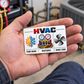 HVAC Minimal Tool Grid aluminum keepsake wallet card lying front-up in an adult worker's open palm in a workshop.