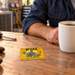 HVAC Golden Milestone aluminum wallet card lying flat on a wooden HVAC workshop break table beside an adult worker's hands and a plain coffee mug.