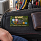 HVAC Rugged Field aluminum keepsake wallet card lying flat on a canvas tool bag beside a leather wallet and an adult worker's hand.