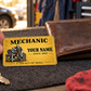 Mechanic Golden Milestone aluminum wallet card shown at wallet scale in an automotive workshop setting.