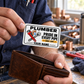 The printed front of the Plumber Honeycomb Pride aluminum wallet card shown in an occupational lifestyle setting with an adult worker.