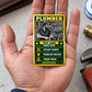 The printed front of the Plumber Trade Legend Collectible aluminum wallet card shown in an occupational lifestyle setting with an adult worker.