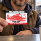 Railroader Red Monochrome aluminum keepsake wallet card held at its corner by an adult worker at a crew break counter.