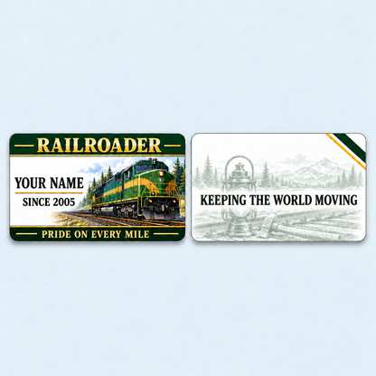 Railroader Heritage Band aluminum keepsake wallet card, front and reverse views. A deep-green header and fine gold-colored rules frame a forest railway scene, with name-and-year lettering to the left of the locomotive. A softly faded lantern-and-tools illustration on the reverse surrounds the message KEEPING THE WORLD MOVING.