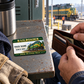 Railroader Heritage Band wallet card lying flat on a depot locker shelf beside an open brown wallet and adult worker's hands.