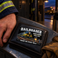Railroader Midnight Pride wallet card lying flat on a dark leather wallet beside a worker's hand in an evening depot locker room.
