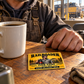 Railroader Golden Milestone wallet card lying flat on a wooden crew-room table beside a coffee mug and an adult worker's hand.