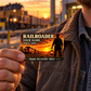 Railroader Sunset Workday wallet card held at chest level by an adult worker at a depot during golden hour.