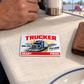 Trucker Signature Classic wallet card on linen at a truck-stop lunch table beside a closed leather wallet