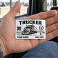 Trucker Minimal Tool Grid aluminum wallet card resting on an adult open palm inside a parked truck