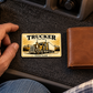 Trucker Golden Milestone wallet card on charcoal felt beside a closed tan wallet in a parked truck cabin