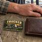 Trucker Rugged Field wallet card on canvas beside a closed wallet and resting hand inside a parked truck