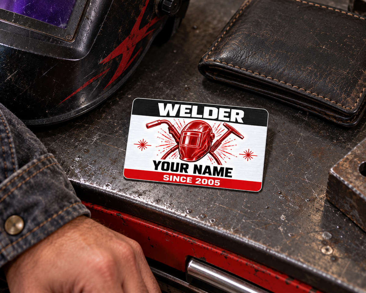 Welder Red Monochrome aluminum wallet card on a toolbox beside a closed wallet and inactive welding hood