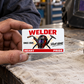 Adult welder holds the Signature Classic wallet card over a linen-covered workshop bench